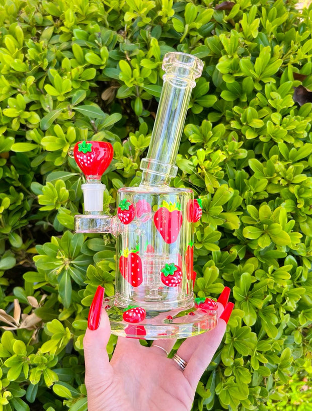 hand holding a strawberry glass pipe against a greenery background outside